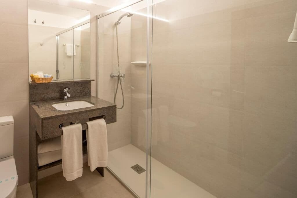Un baño moderno con ducha envuelta en vidrio, lavabo con encimera de granito y retrete a la vista.
