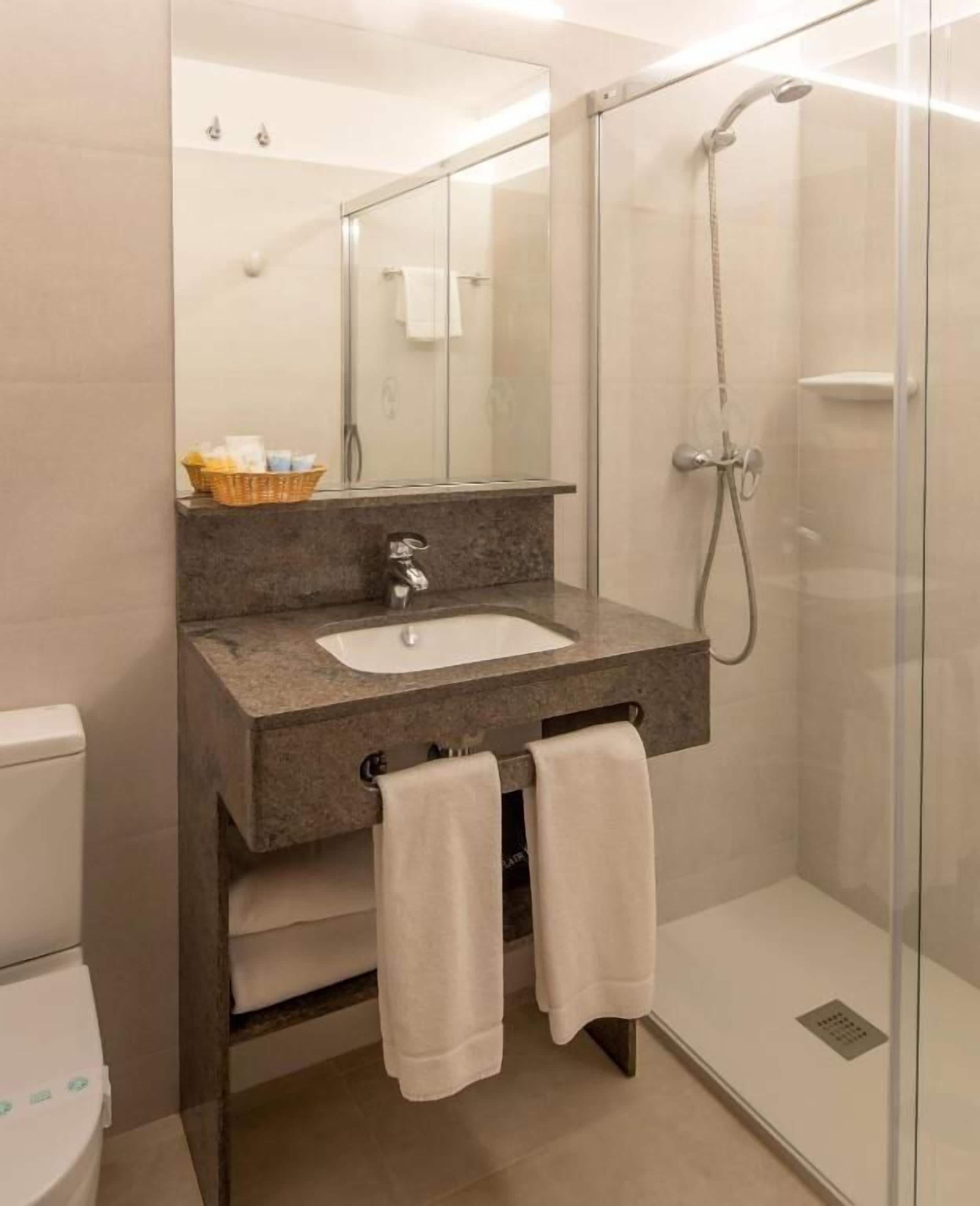 A modern bathroom with a glass-enclosed shower, a granite countertop sink, and a mirror above it.