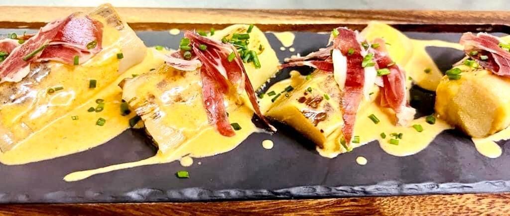 Un plato con carne en rodajas y salsa cremosa, adornado con cebollines sobre un plato oscuro.