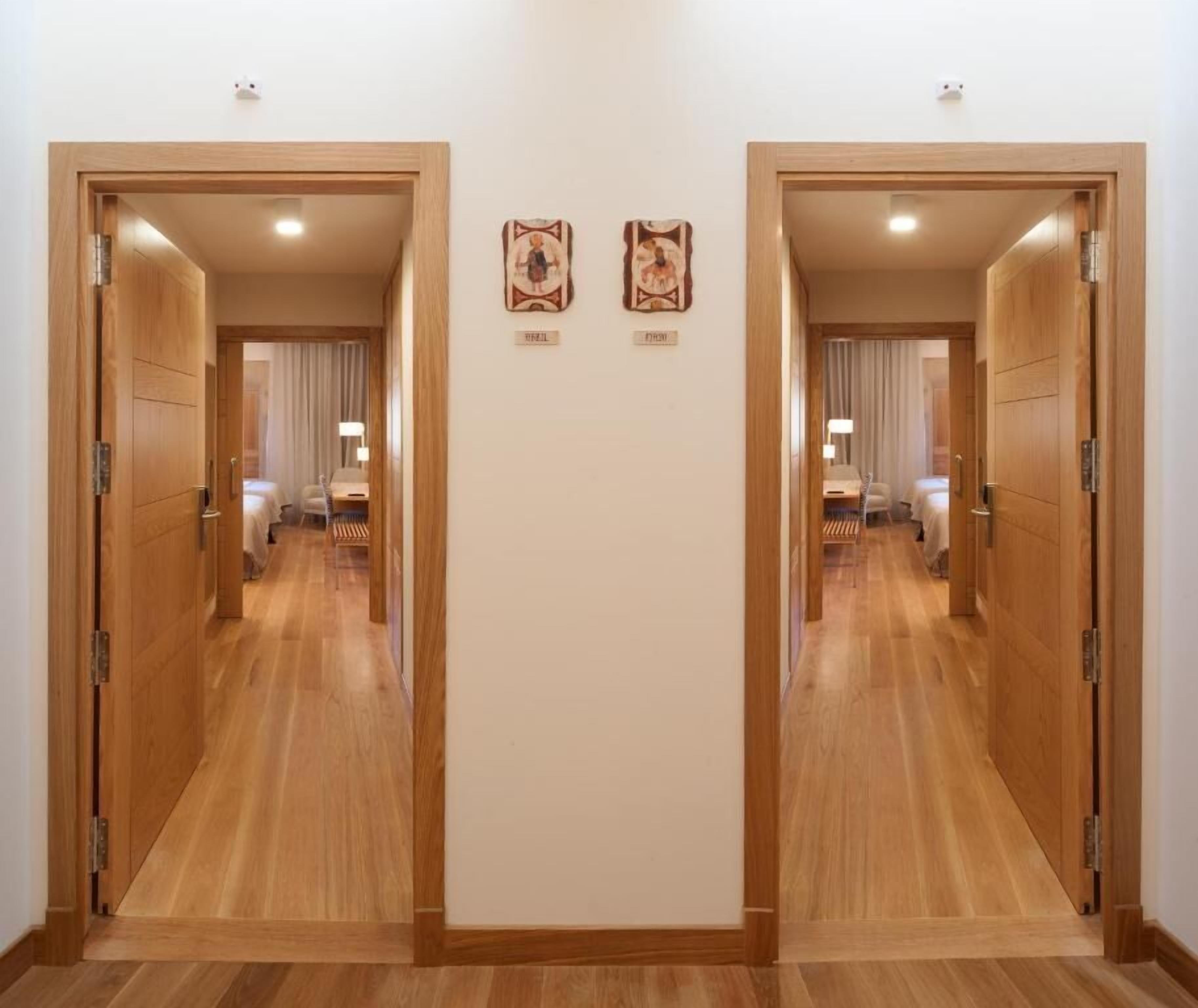 A hotel corridor with wooden flooring and doors leading to rooms. There are two framed pictures on the wall.