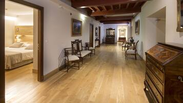 A spacious room with wooden flooring, a bed, several chairs, a dresser, and a hallway leading to another room.