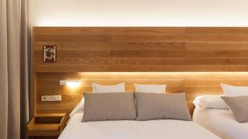 Habitación de hotel moderna con cabecera de madera, mesita de noche y cama con ropa blanca y varios almohadones.