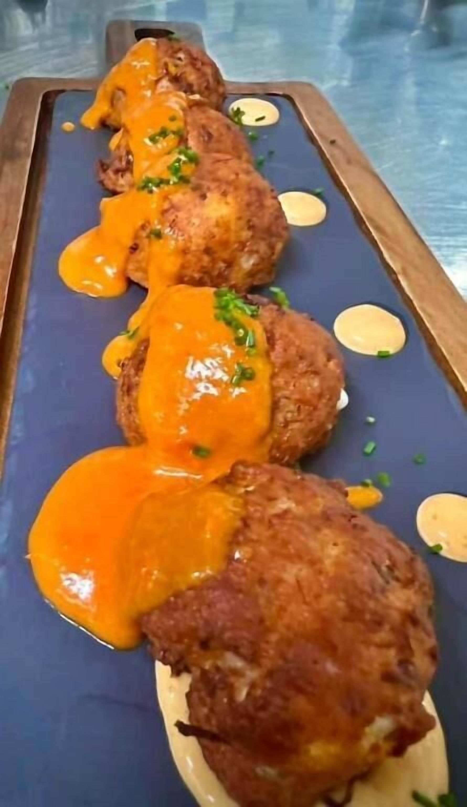 A dish with breaded items topped with orange sauce and garnished with green herbs.