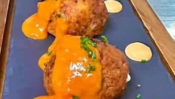 A dish with breaded items topped with orange sauce and garnished with green herbs.