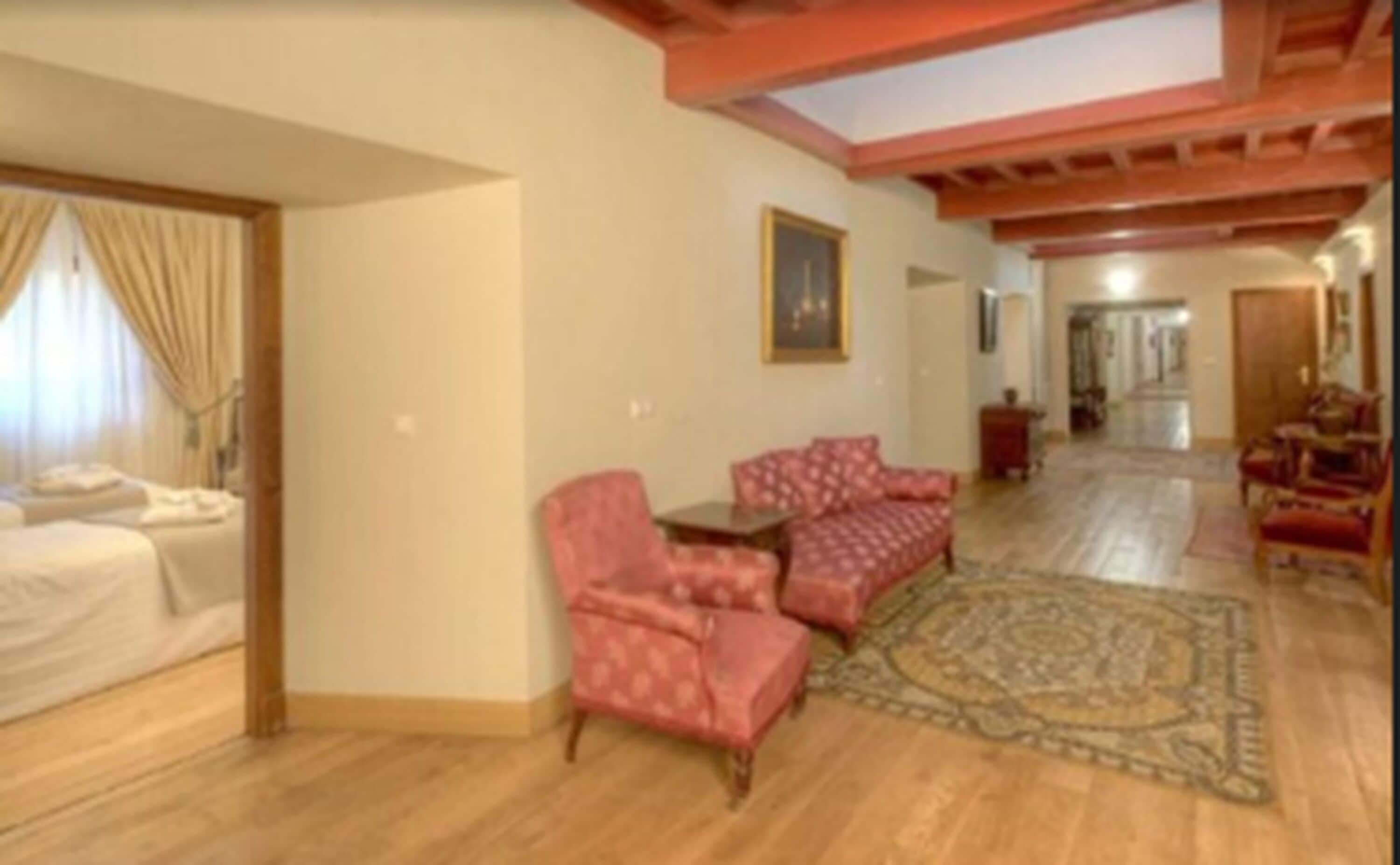 Amplia sala de estar con piso de madera, alfombra estampada y mobiliario tapizado en rojo.