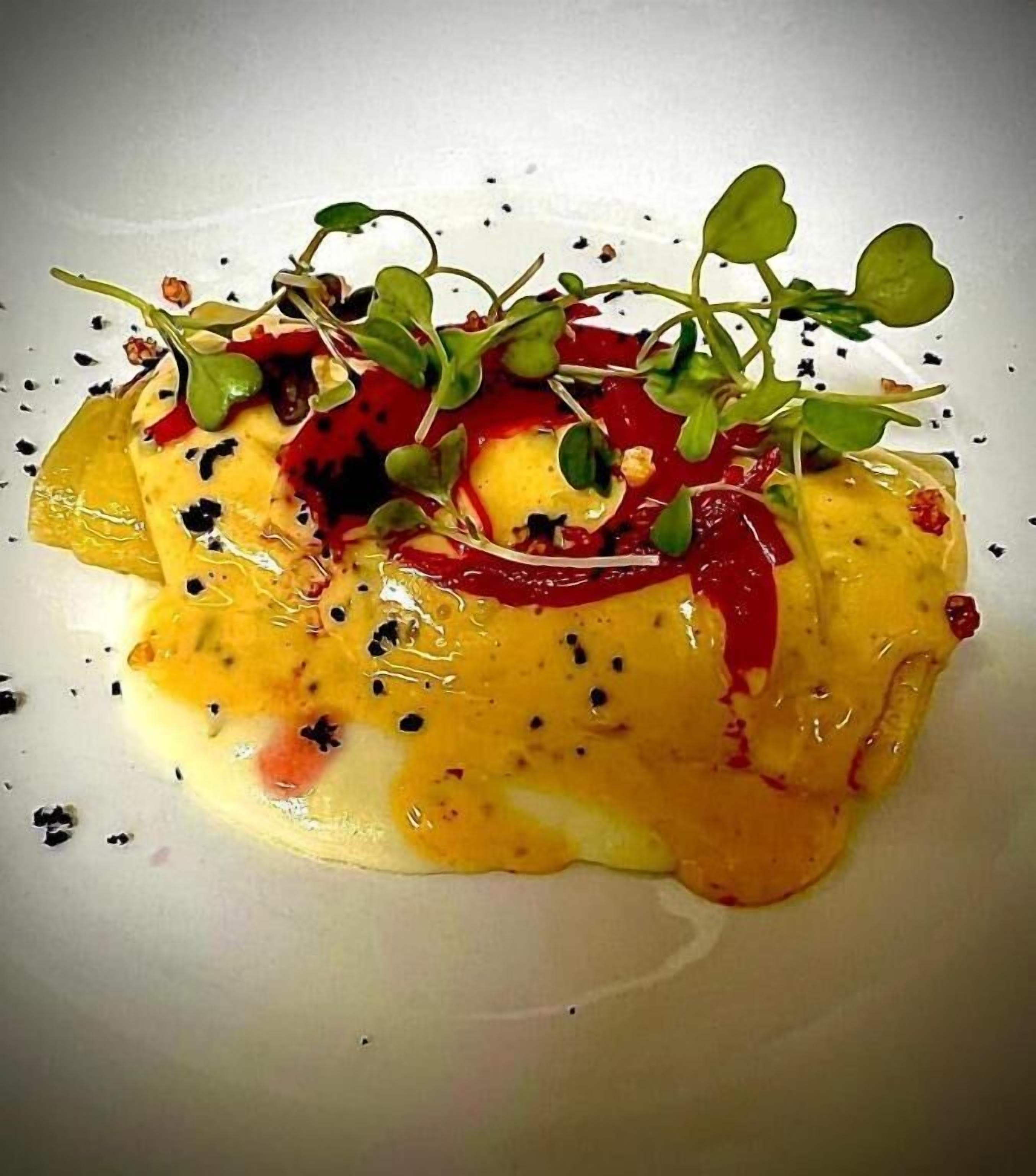 Un plat nappé d’une sauce crémeuse, garni de jeunes pousses et d’une sauce rouge.