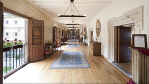 A corridor with wooden flooring, blue patterned rugs, and a view of a building through a glass door. - Hotel Real Colegiata San Isidoro (León)