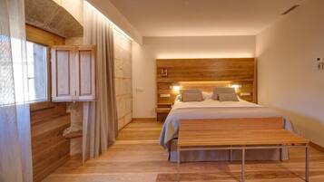 Un dormitorio moderno con cabecera de madera, una cama grande, un banco y una ventana con cortinas.