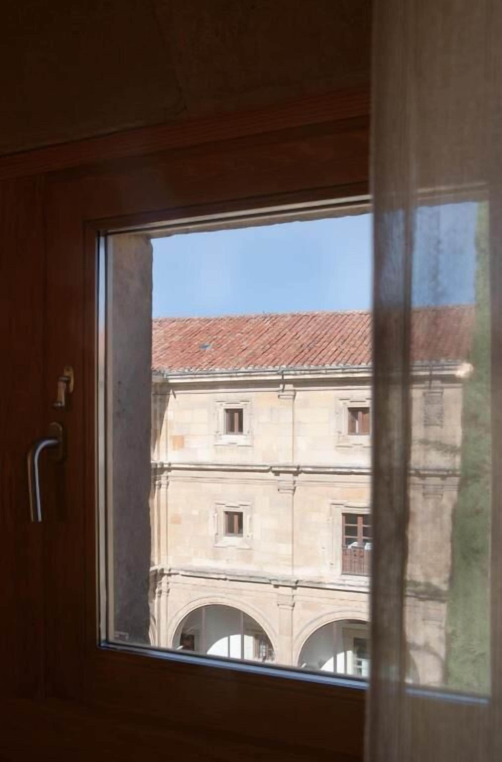Una ventana con vistas a un edificio de techo con tejas y ventanas de arco.