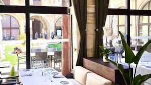 A dining area with a table set for four, large arched windows, and a view of a historic building. - Hotel Real Colegiata San Isidoro (León)