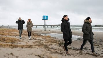 Una spiaggia con un molo sullo sfondo, un cartello con il numero 9 e persone che passeggiano lungo la riva.
