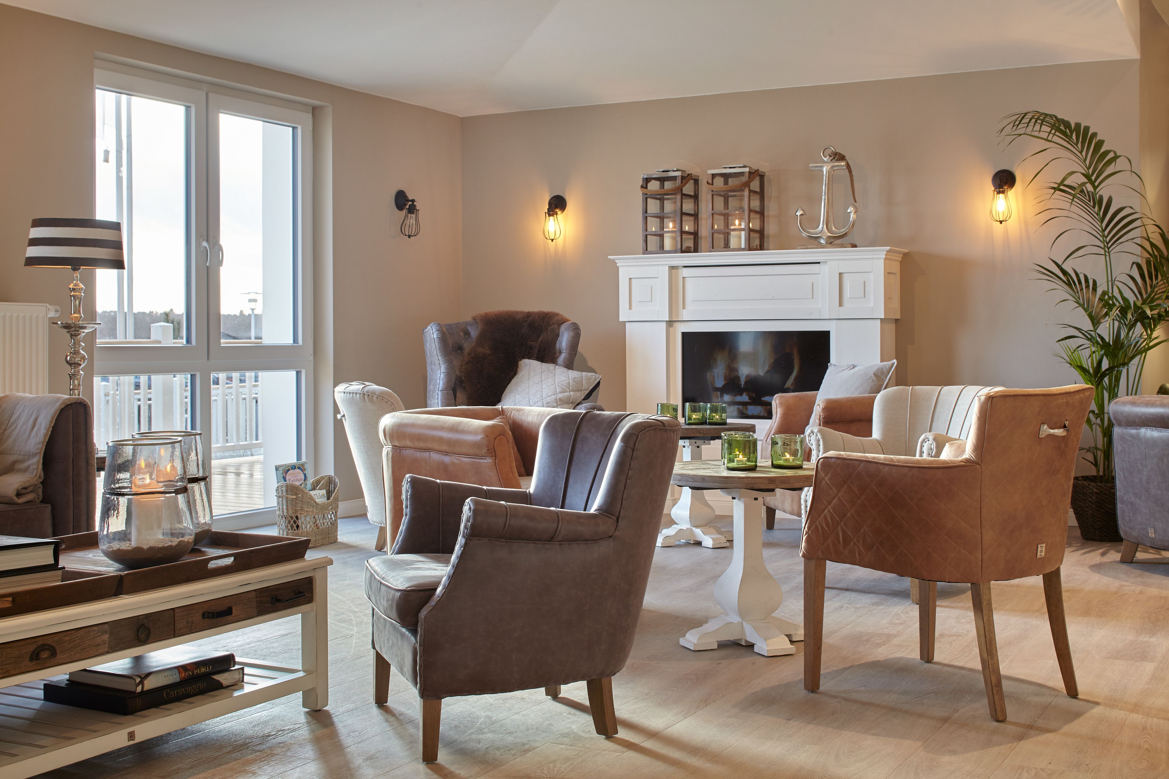 Ein Wohnzimmer mit Kamin, Ledersesseln, einem Couchtisch mit Büchern und einem großen Fenster.