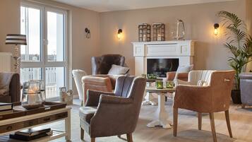 Ein Wohnzimmer mit Kamin, Ledersesseln, einem Couchtisch mit Büchern und einem großen Fenster.