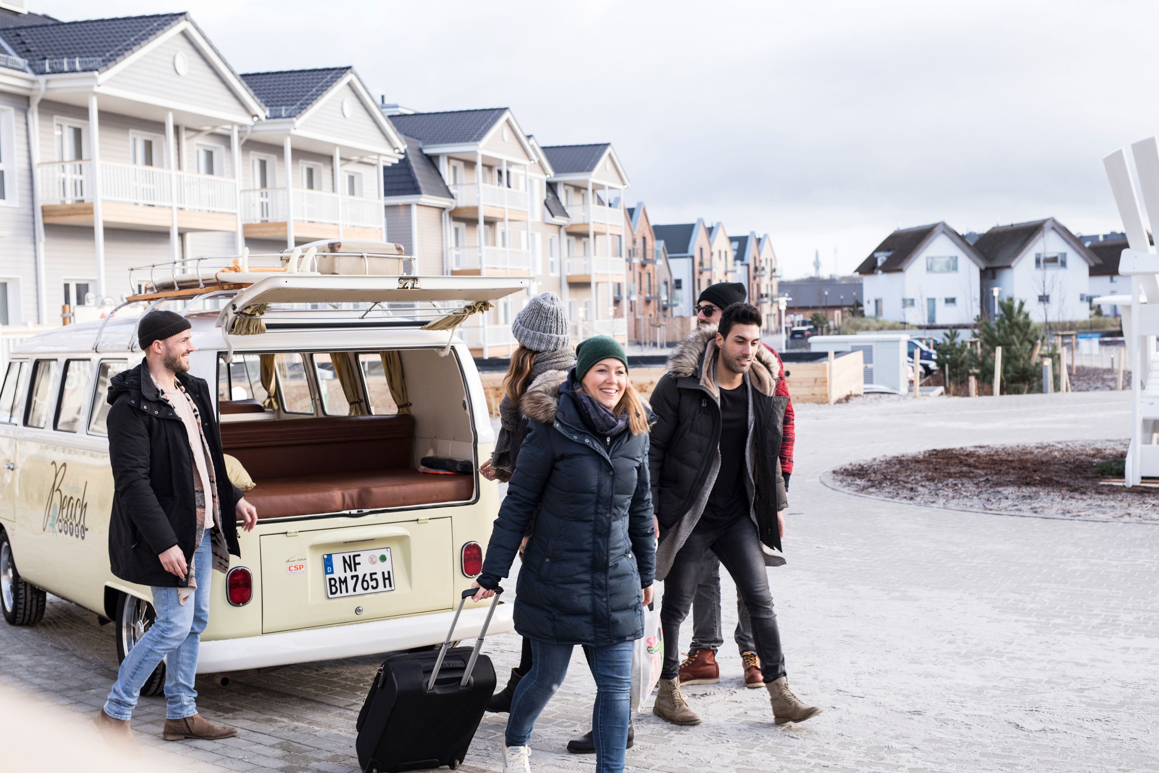 A group of people walking past a white van with a brown interior and a license plate.
