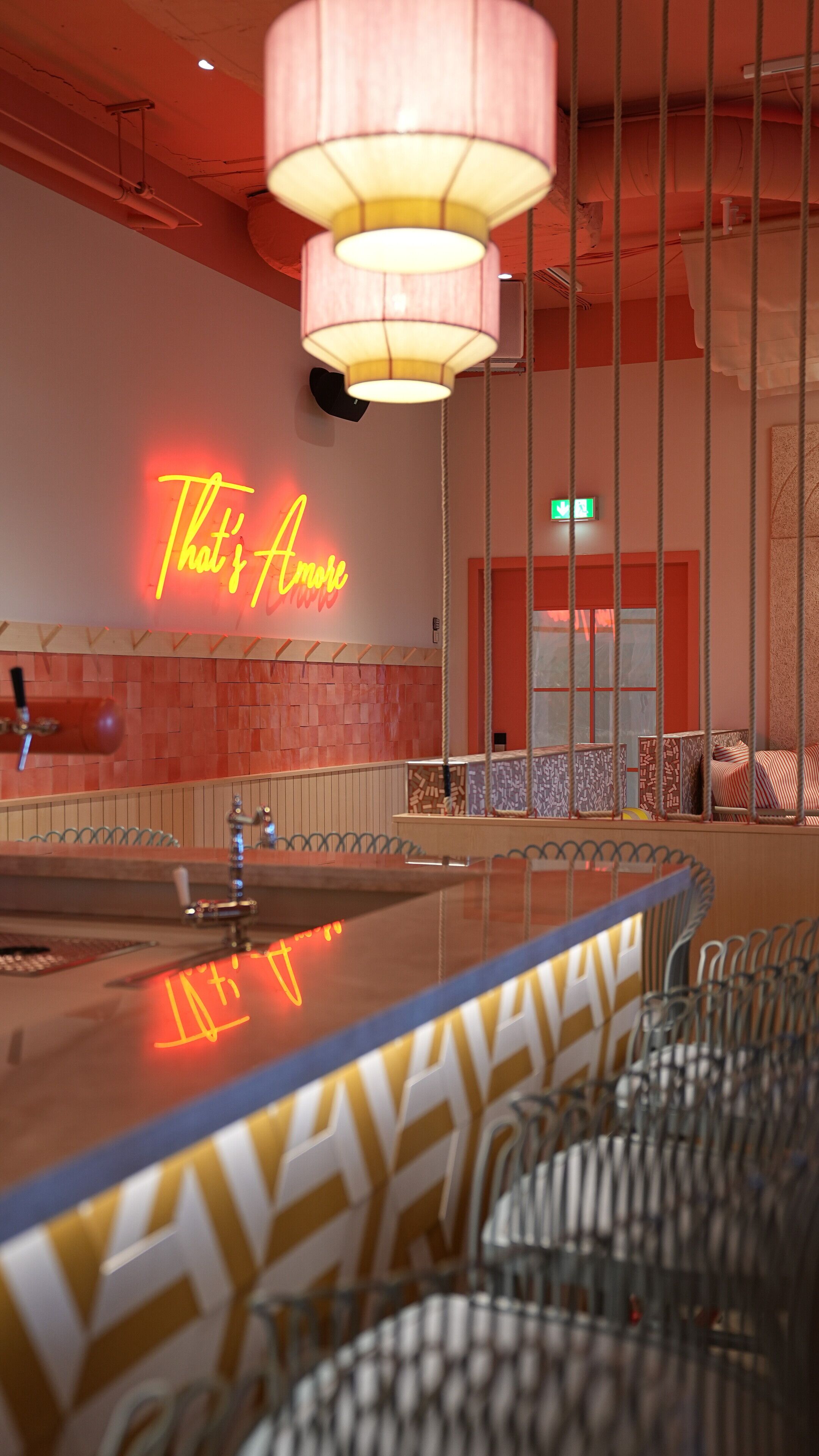 Un'area bar con un neon che riporta la scritta “That's All”, un lampadario e una zona con sedute caratterizzate da un motivo decorativo.