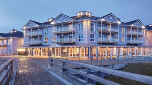 Un hotel de varios pisos con balcones, un área de estar al aire libre cubierta y vista al agua.