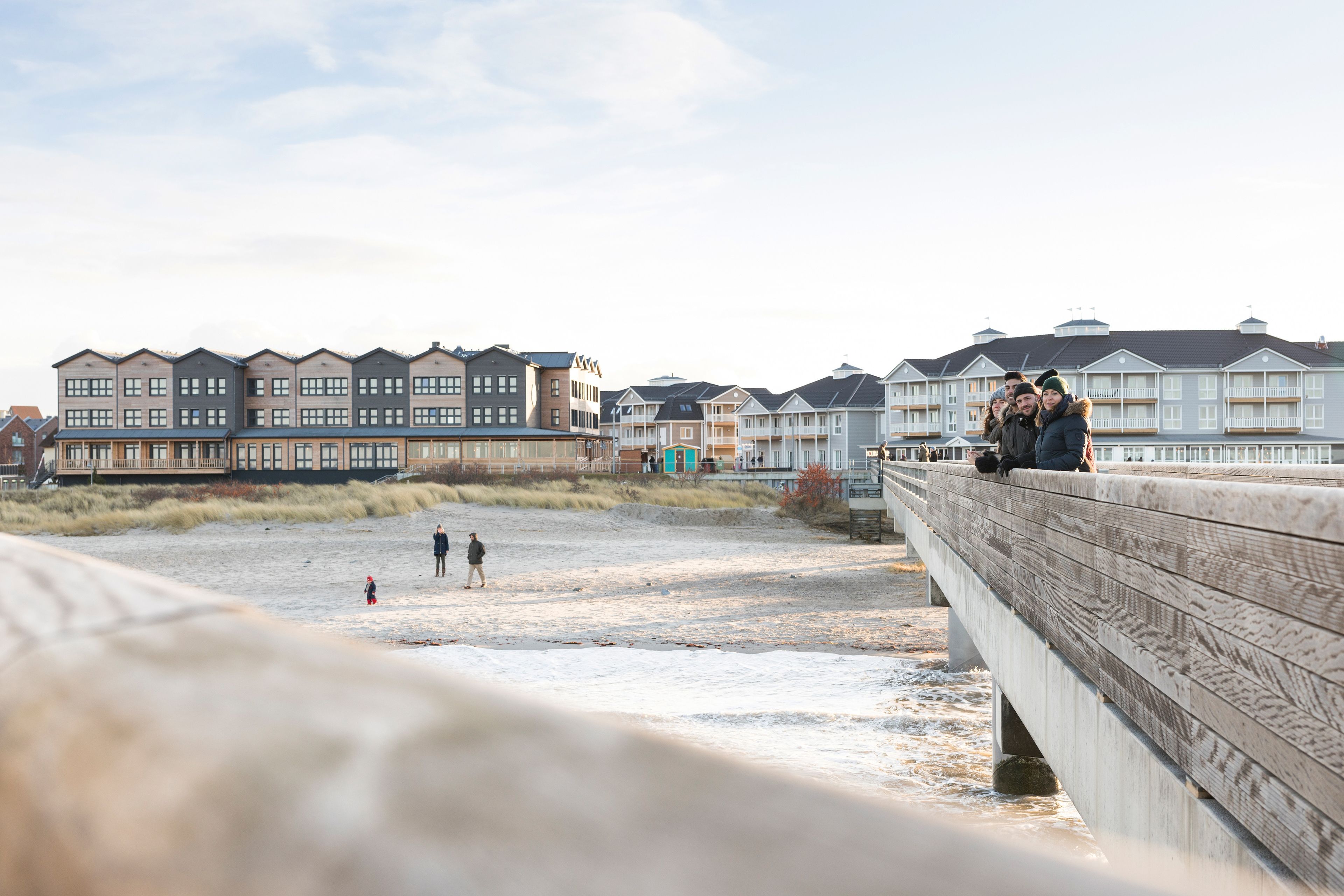 A coastal hotel with multiple buildings, a sandy beach, and a wooden bridge.