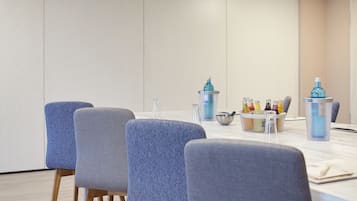 Een vergaderruimte met een lange tafel, vier grijze bekleden stoelen en een waterdispenser.