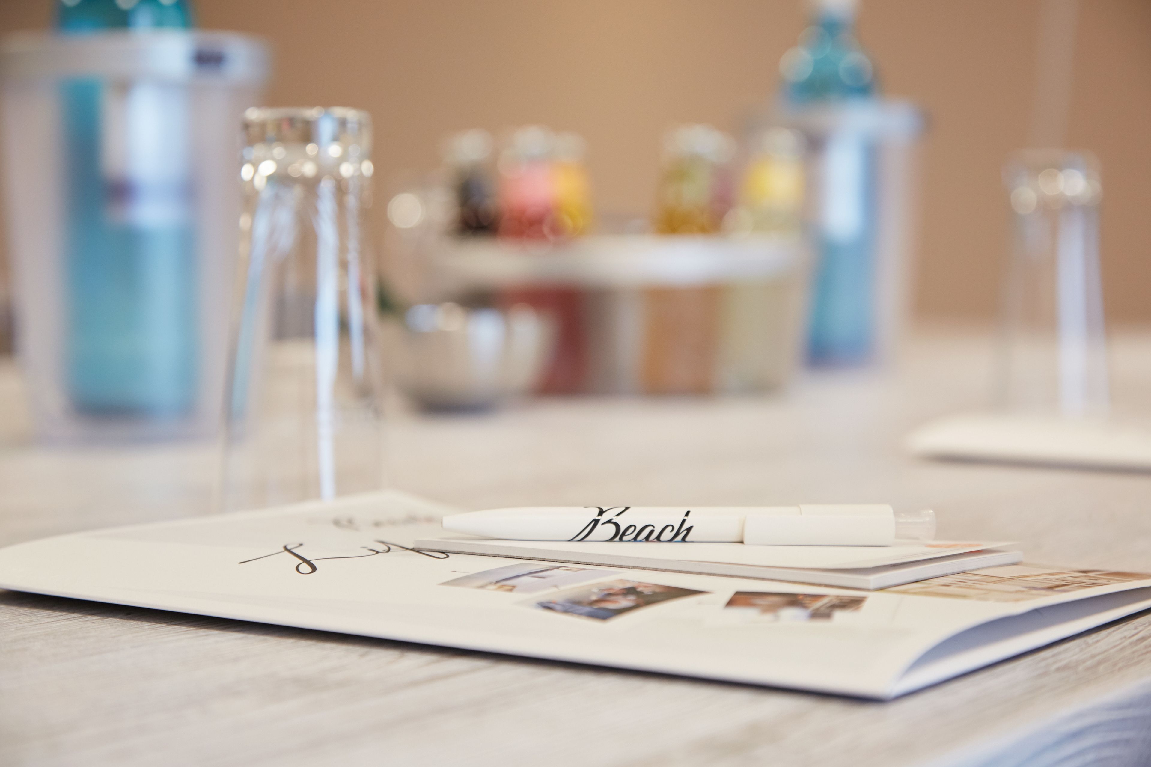 A table with a notebook, a pen, and a glass with a name tag that reads "Beach".