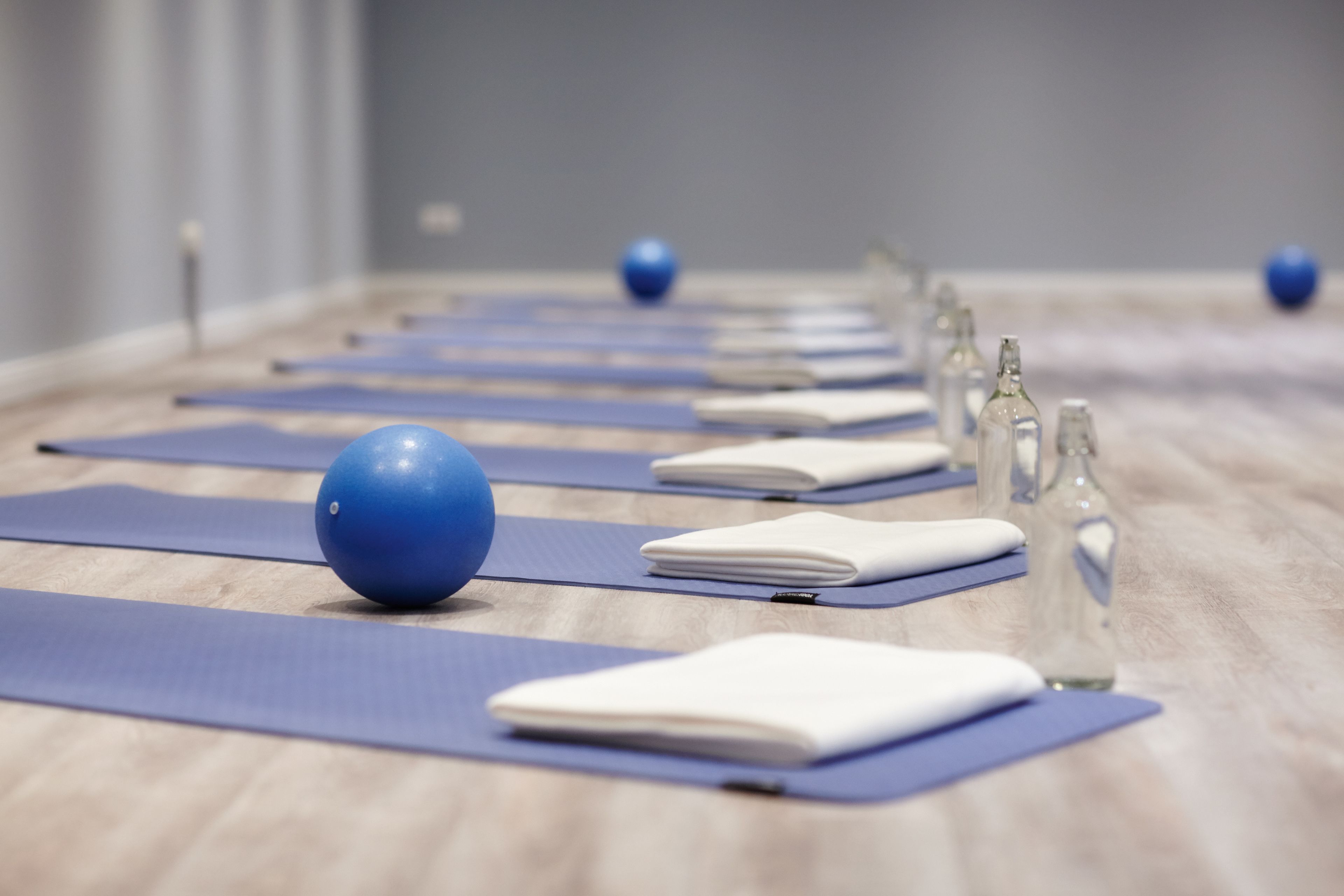 A row of yoga mats with blue balls and water bottles on a wooden floor.