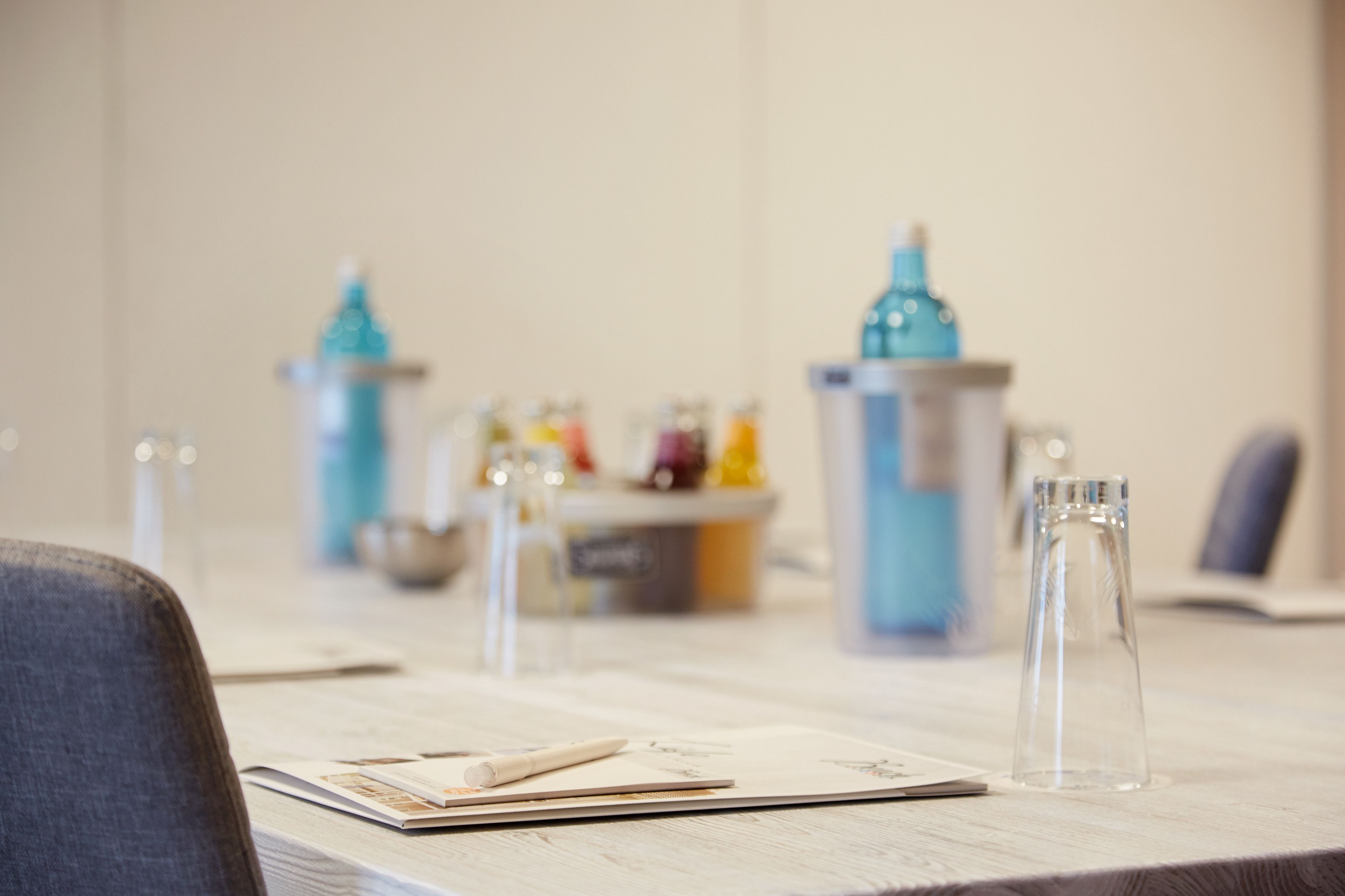 Una mesa con un cuaderno, bolígrafo y vaso. Se observan objetos decorativos al fondo.
