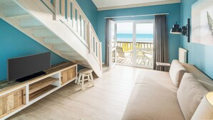 Una sala de estar con televisor, sofá, escalera y balcón con vista al mar.