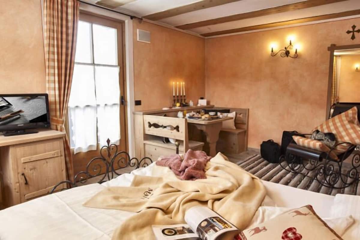 Una habitación de hotel con cama, escritorio, silla, televisión y ventana con cortinas.