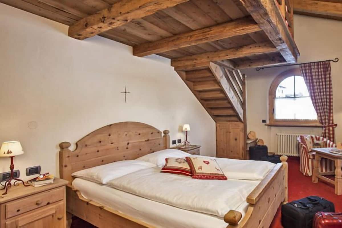 Un dormitorio con una cama de madera, una mesita con sillas, una ventana con cortinas y un radiador.