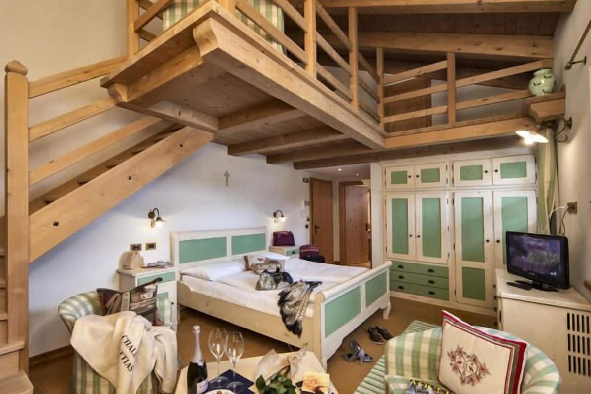 Un dormitorio con cama tipo loft, escritorio, televisor y armario.