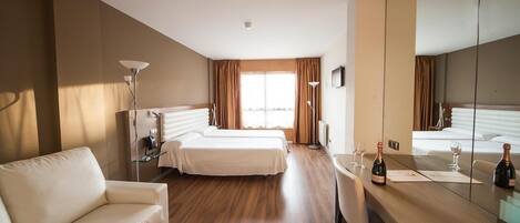 Ein Hotelzimmer mit Holzboden, einem weißen Sofa, zwei Einzelbetten, einem Schreibtisch mit Stuhl und einem großen Spiegel.