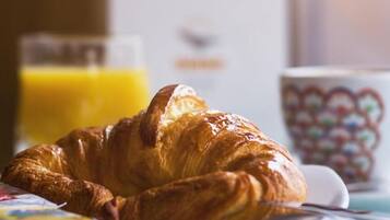 A croissant on a plate with a glass of orange juice and a cup in the background.