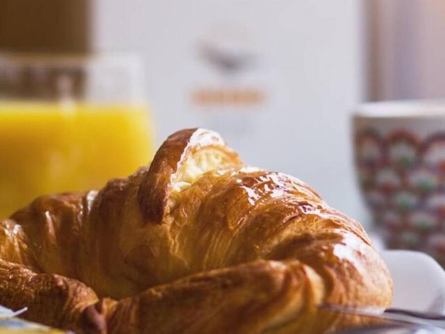 A croissant on a plate with a glass of orange juice and a cup in the background.