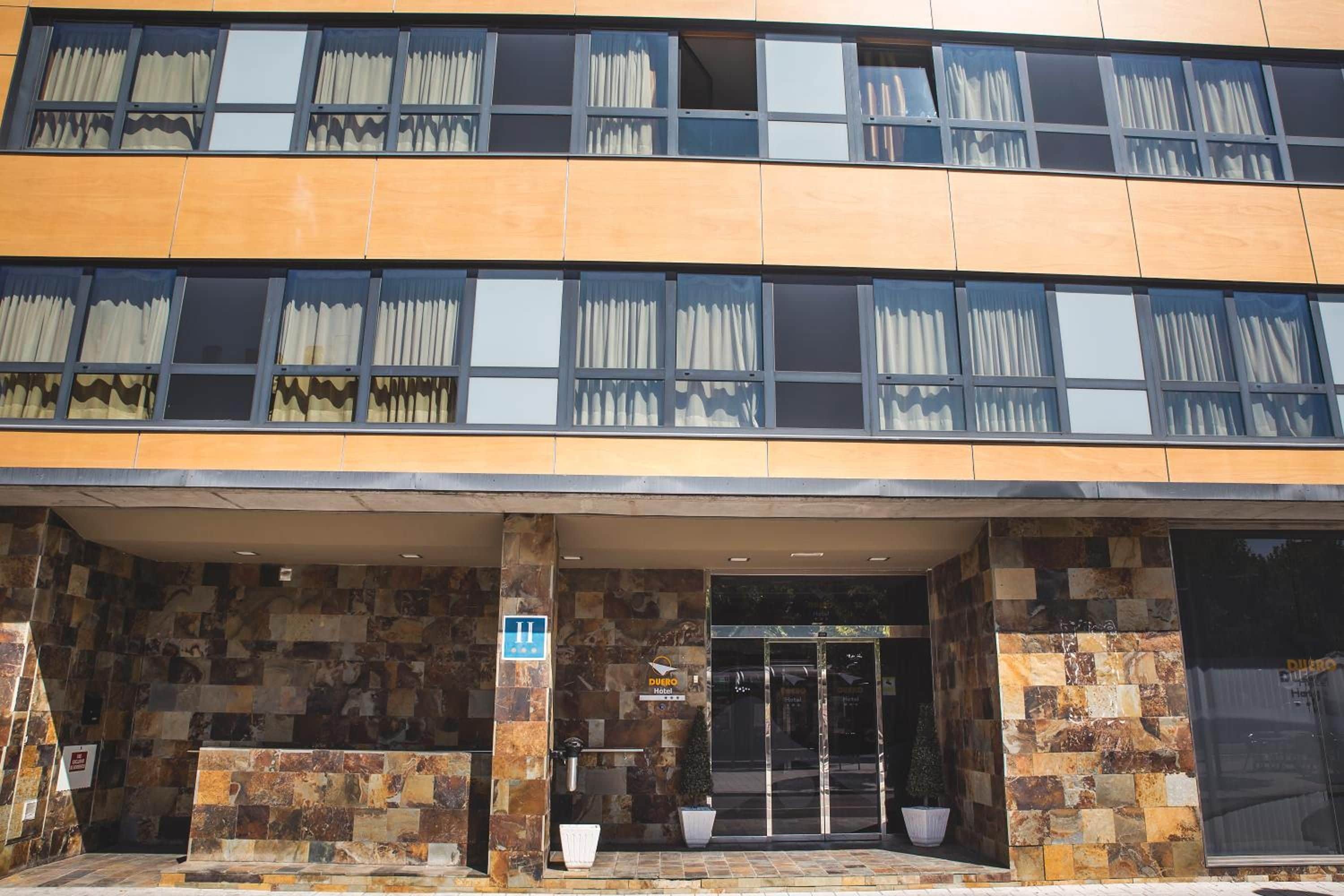A hotel entrance with a stone facade, large windows, and a sign indicating the hotel name.