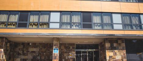 A hotel entrance with a stone facade, large windows, and a sign indicating the hotel name.