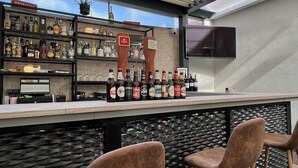 An outdoor bar area with a counter displaying various bottles, a television, and a wooden ceiling. There are three brown chairs with wooden legs. - Duero Hotel (Laguna de Duero)