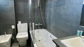 A modern bathroom with a shower, toilet, bidet, and two sinks.