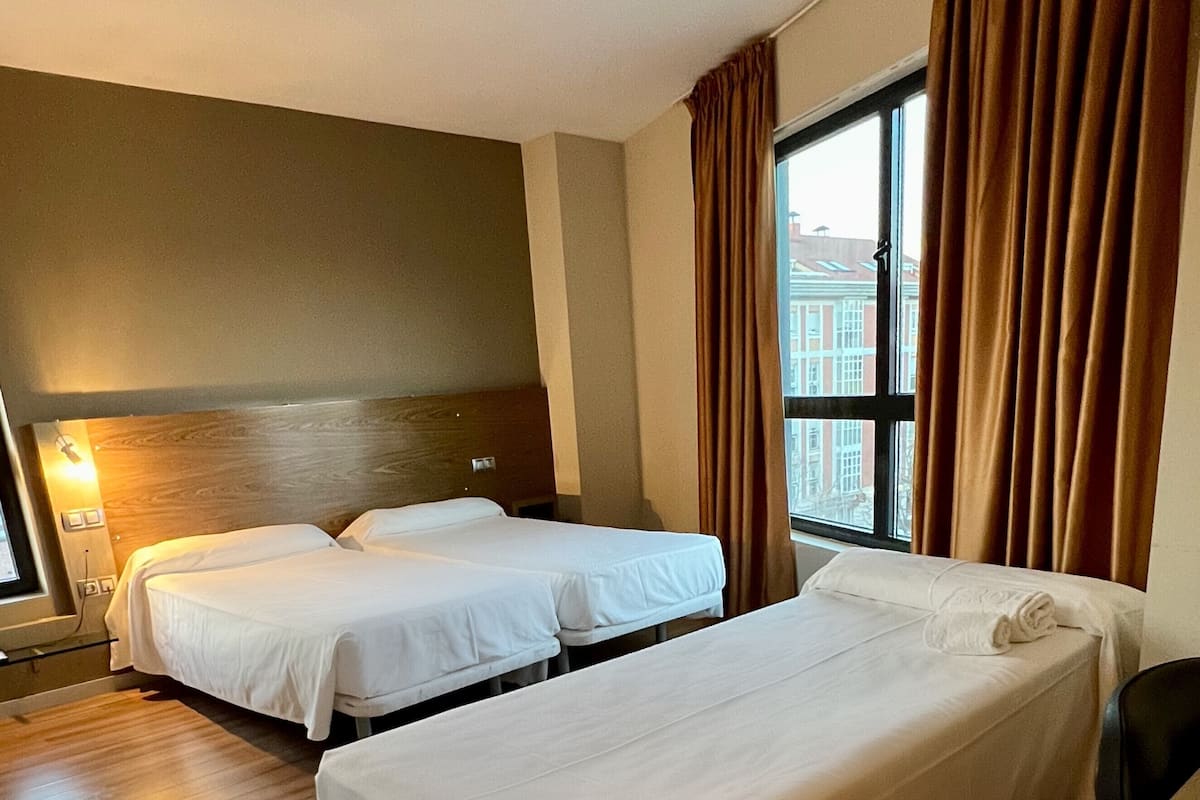 Une chambre d’hôtel avec deux lits simples, un plancher en bois, une grande fenêtre avec des rideaux et un bureau.