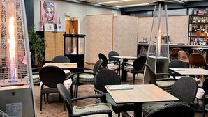 A restaurant with wicker chairs, tables, a fire feature, and a wall with a geometric pattern. - Duero Hotel (Laguna de Duero)