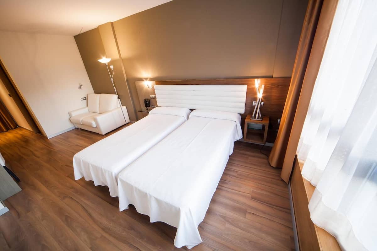 Une chambre d’hôtel avec un grand lit, une chaise, une table de chevet et une lampe.