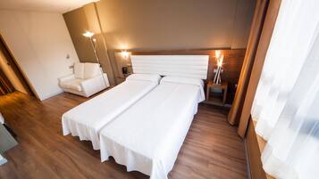 Una habitación de hotel con una cama grande, mesitas de noche, una silla y una lámpara.