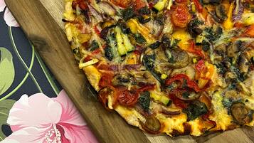Pizza sobre tábua de madeira com toalha de mesa florida.