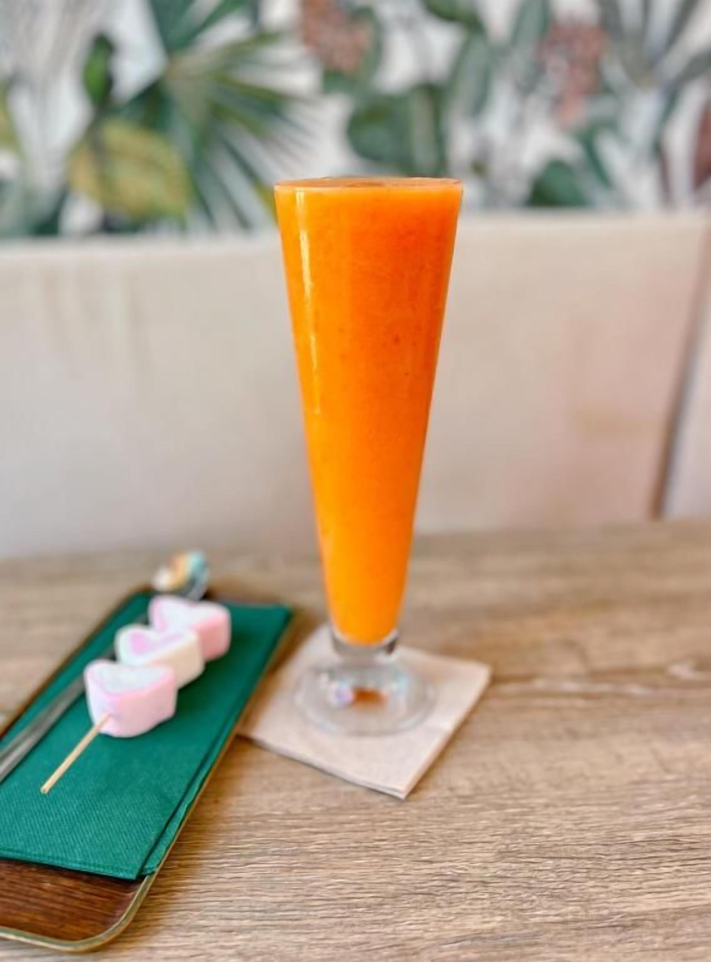 A glass of orange juice on a wooden table with a green napkin and pink heart-shaped items.