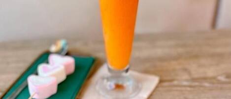 A glass of orange juice on a wooden table with a green napkin and pink heart-shaped items.