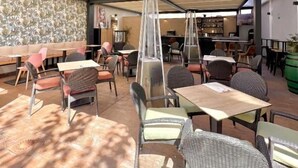Een terras met tafels en stoelen, een pergola erboven en uitzicht op het interieur.