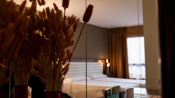 A hotel room with a bed, bedside table, and a vase with dried flowers. - Duero Hotel (Laguna de Duero)