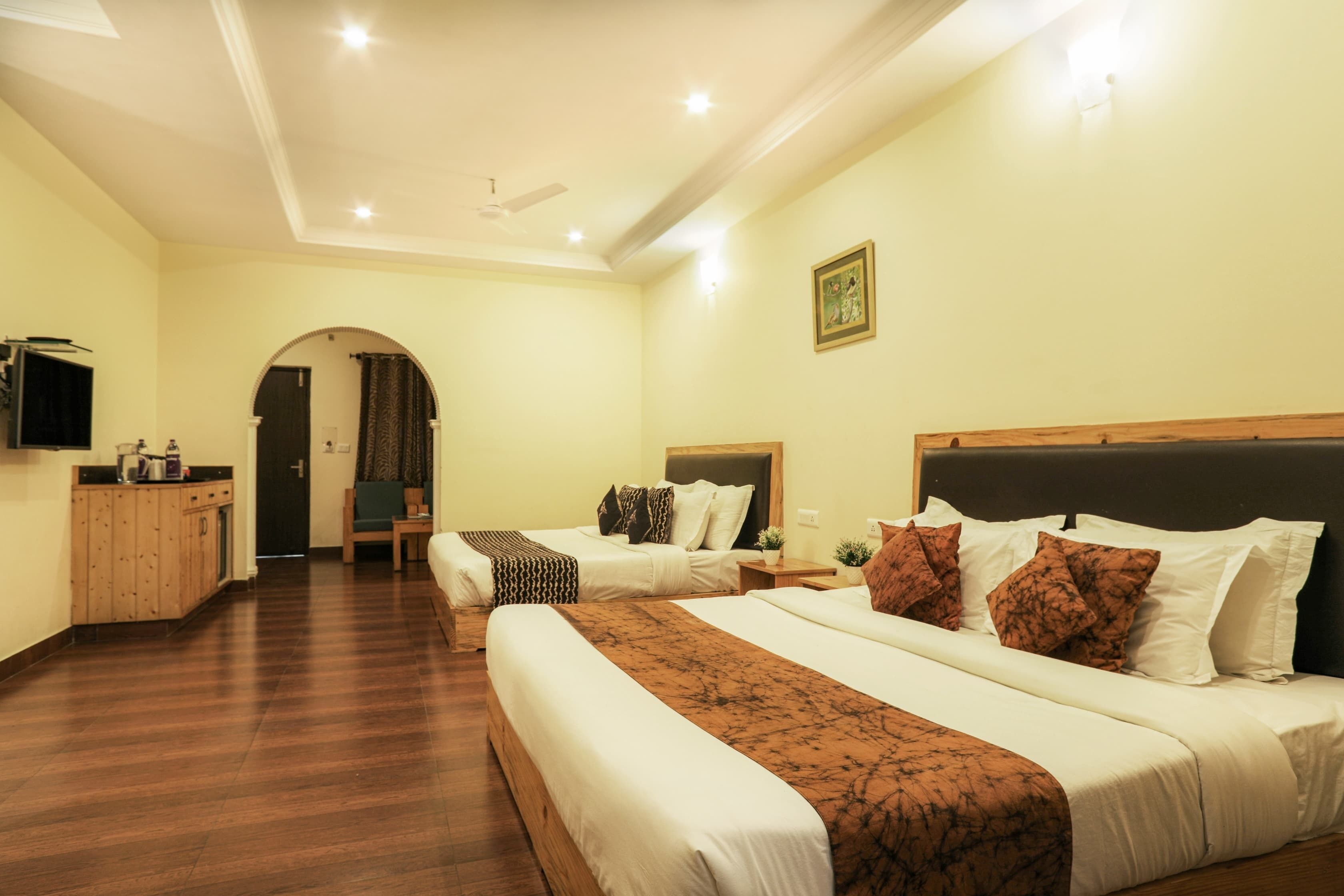 A hotel room with two beds, a TV, a desk, and a bathroom visible through an archway.