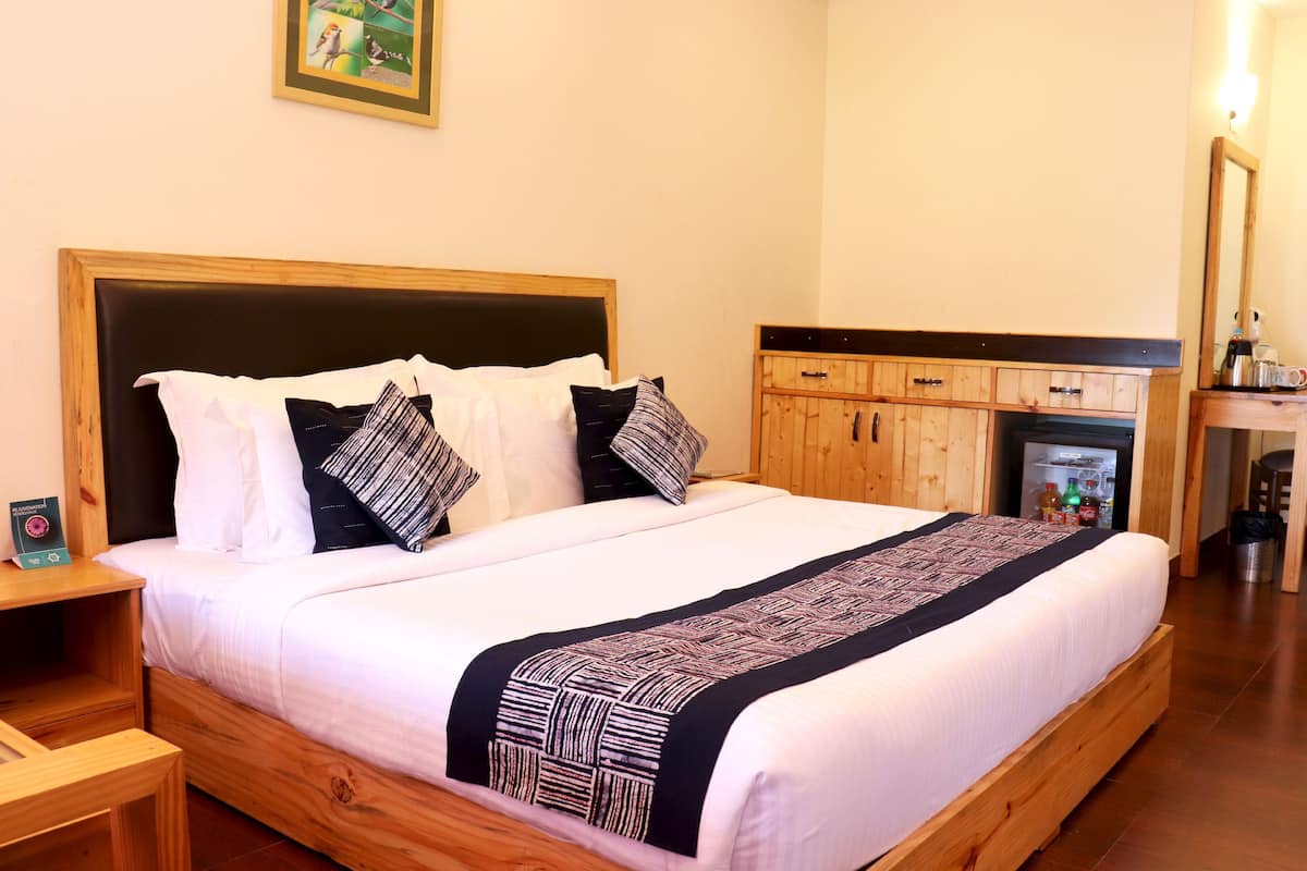 A neatly made bed with a wooden headboard, a bedside table, and a small cabinet with a refrigerator.