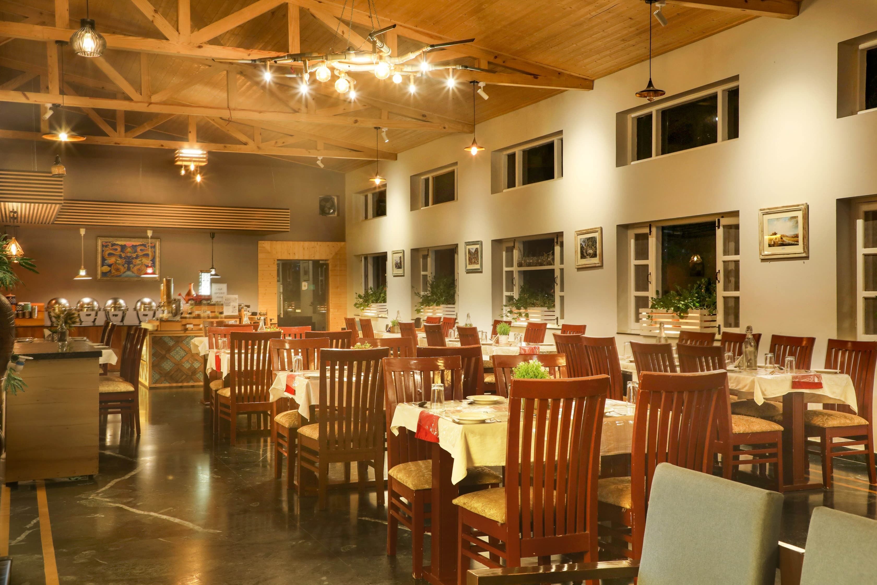 A spacious dining area with multiple tables and chairs, wooden ceiling beams, and pendant lighting.