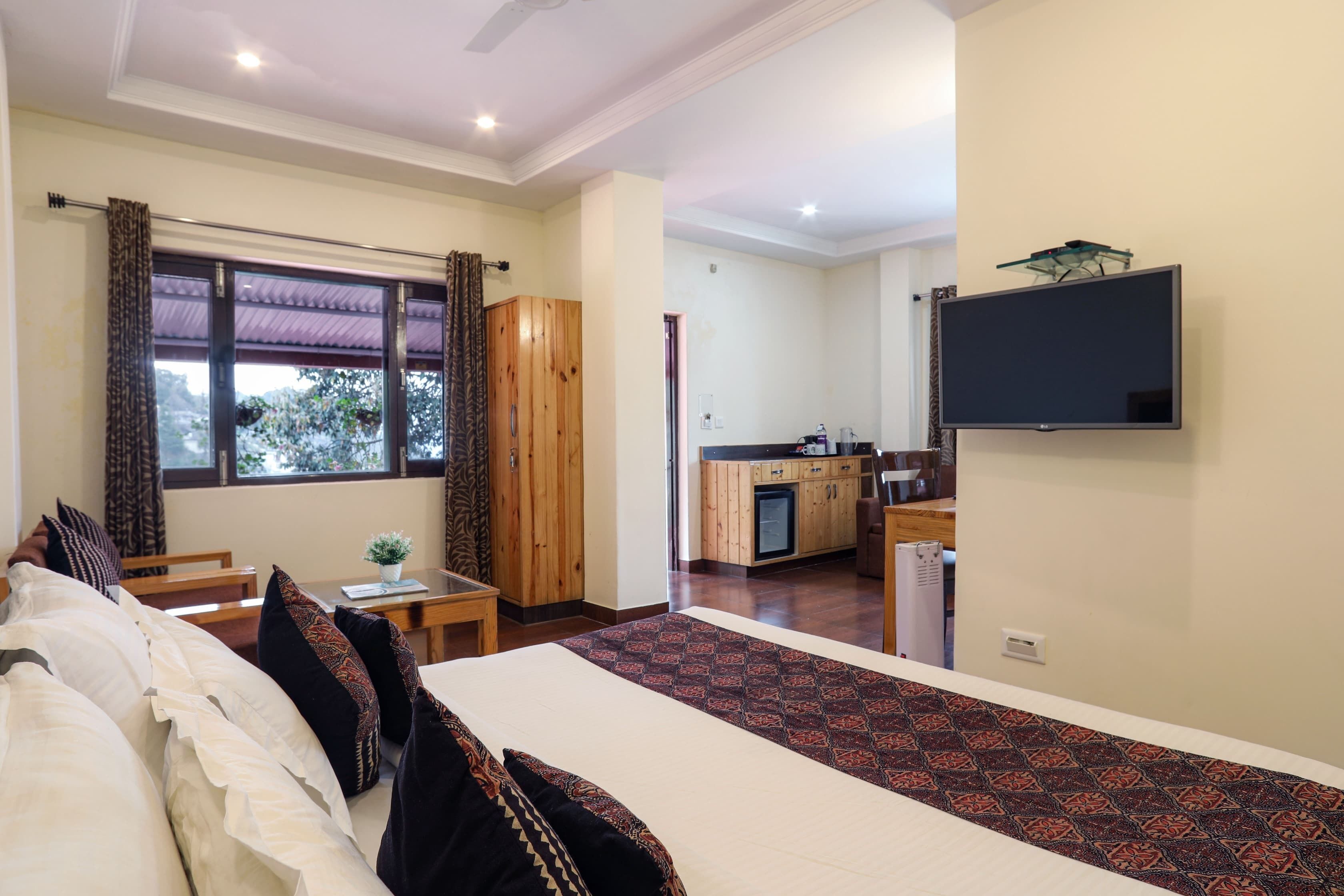 A hotel room with a bed, a desk, a chair, a TV, and a kitchen area.