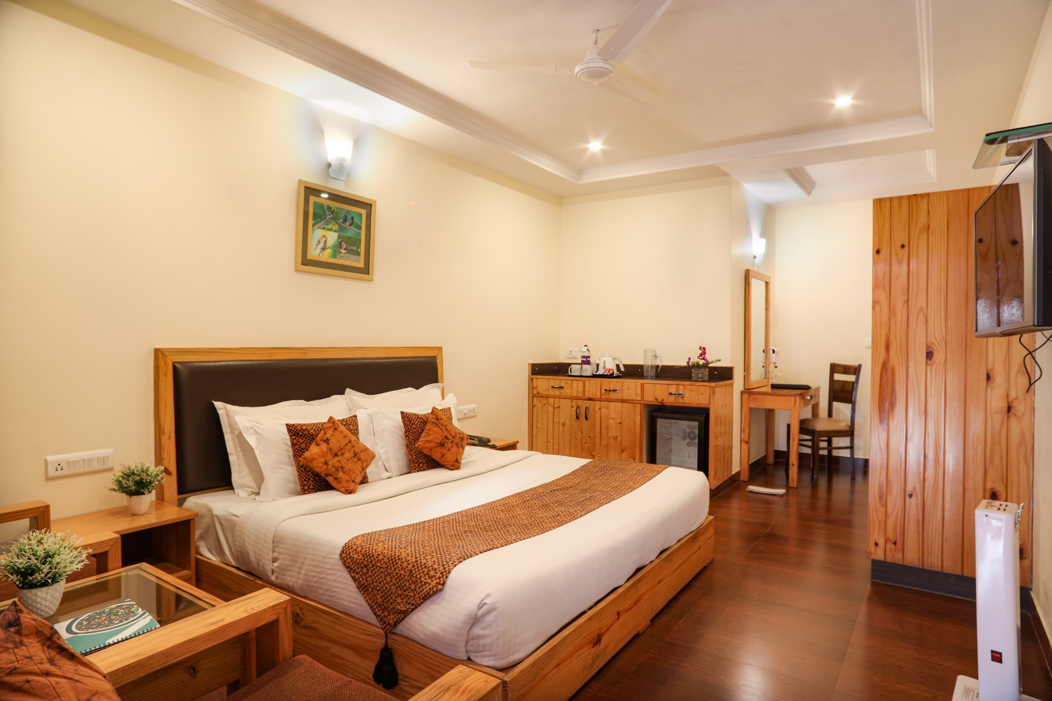 A hotel room with a large bed, wooden headboard, bedside tables with lamps, a desk, and a television.